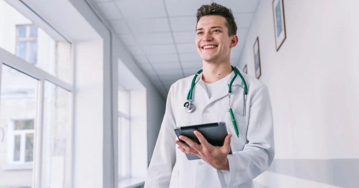 Médico sorridente com jaleco, estetoscópio e tablet em um ambiente de hospital, representando o artigo sobre Simples Nacional para médico.