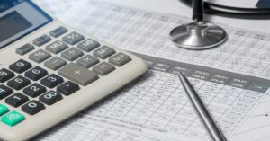 Calculadora, estetoscópio e caneta sobre planilha financeira, representando o planejamento tributário para médicos.