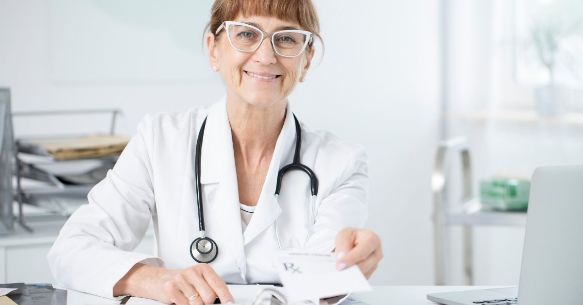 Médica sentada em sua mesa, com o recibo médico em mãos, apontando para alguém que está à sua frente