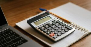 Calculadora sobre um caderno ao lado de notebook, representando como calcular o Fator R no Simples Nacional para clínicas e consultórios médicos.